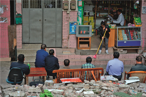 2015年11月28日，冼村也成为不少外来民工的落脚地，人们坐在一家小卖部前围观电视。