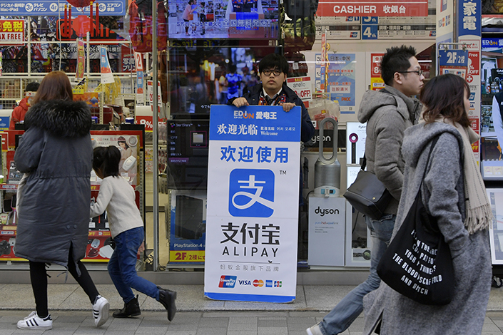 Ant Financial Services Group is forging partnerships in Asia, Europe and the U.S. in an ambitious bid to connect its payment service, Alipay, with more customers and merchants globally. Above, a store employee holds a billboard promoting Alipay in Akihabara area of Tokyo on Jan. 29. Photo: Visual China