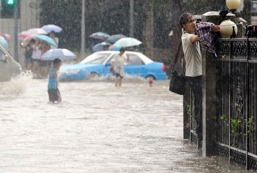6月18日，武汉大学门前积水严重，行人攀着围墙前行。 双木/东方IC  _暴雨袭击武汉 市内交通几近瘫痪