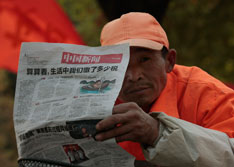 2010年11月20日，南京街头阅读报纸上税收报道的环卫工人。