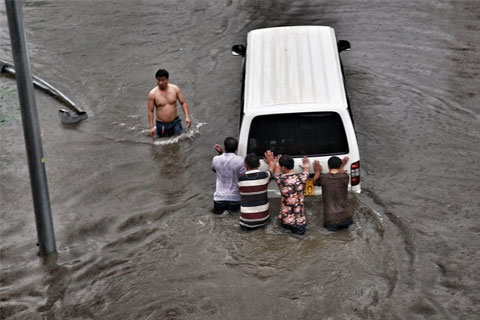 A group tries to push their vehilce marooned in a flooded area in downtown Beijing on July 20