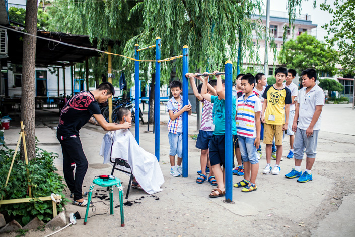 A teacher cuts a student's hair while other students wait outside their school, which caters to migrant workers' children, in Beijing on July 15, 2015. Photo: Visual China