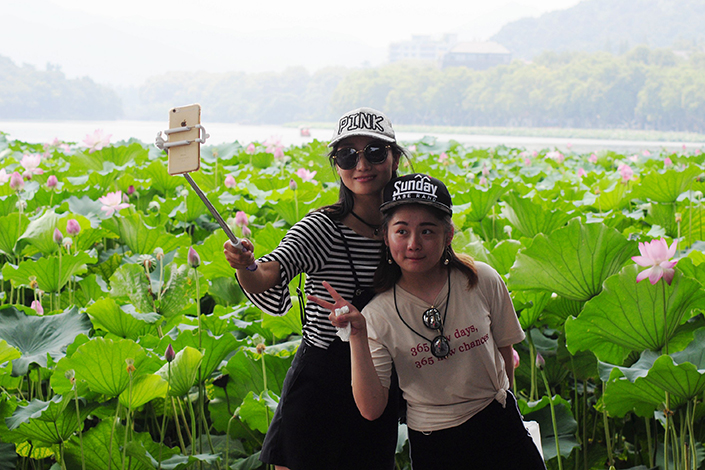 Online travel agency Ctrip is seeking to grow its market share in a tourism market dominated by entrenched offline opponents.  Above, two Hangzhou visitors take a selfie in front of lotus at West Lake in Hangzhou, Zhejiang province, on July 28. Photo: IC