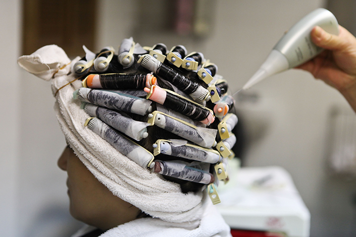 A hair stylist curls a woman's hair in a salon in Shanghai on July 10, 2012. Photo: Visual China