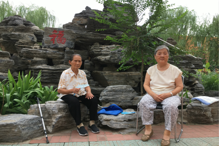 Two women sit in front of an artificial mountain at the Laowulao Elder Care Facility in Beijing's Fengtai district in July. Photo: Cecilia Chang/Caixin