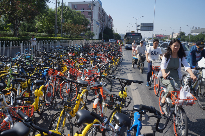 Commuters cycle past shared bicycles parking along the street in Beijing on Aug. 2. Several cities have asked bike-sharing companies to stop putting additional bikes onto city roads. Photo: Visual China.