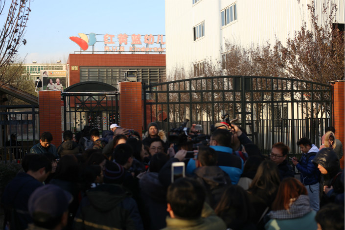Parents and reporters crowd together Thursday outside the Beijing kindergarten accused of abusing children. The company that runs the facility directly operated 80 kindergartens and franchised another 175 preschools, in 130 cities and towns across China, as of June 30. Photo: Caixin