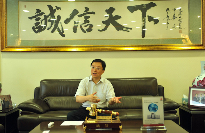 Dagong Chairman Guan Jianzhong sits beneath a work of calligraphy that reads 