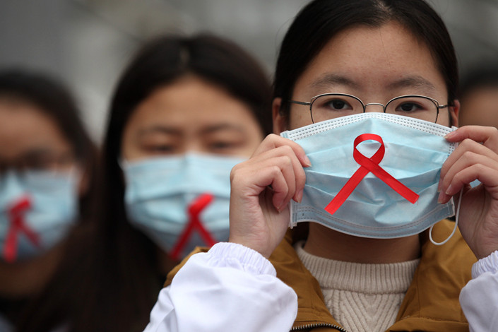 University student volunteers wear red ribbons on Nov. 30 to promote HIV/AIDS awareness at the medical college of Yangzhou University in East China’s Jiangsu province. Photo: VCGc