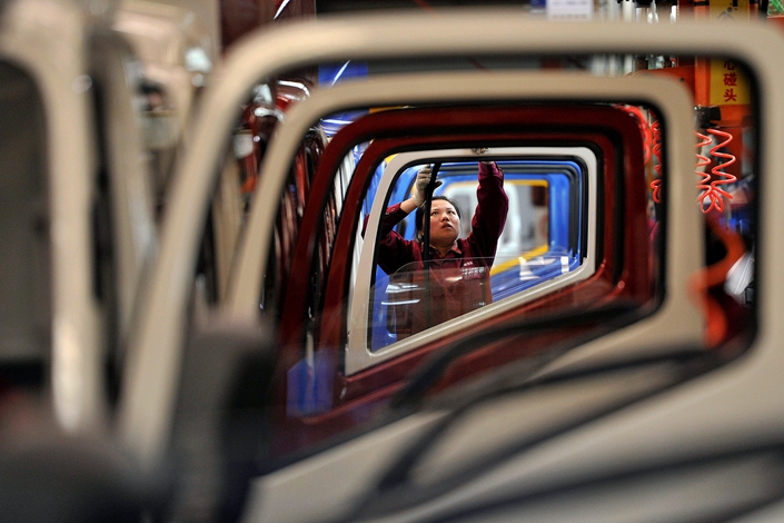 A worker installs rubber onto the windows of vehicle doors on a truck factory production line at JAC Motors in Hefei, Anhui province, July 5, 2019. Photo:VCG