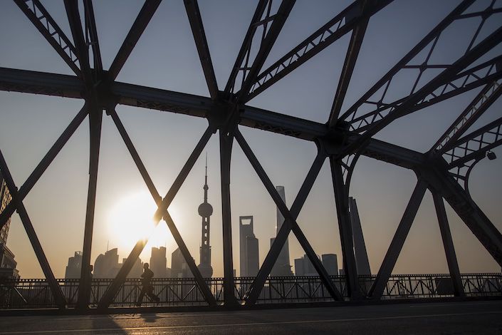 TOPSHOT - A jogger runs across a bridge on his morning exercise during sunrise at the promenade on the Bund along the Huangpu River