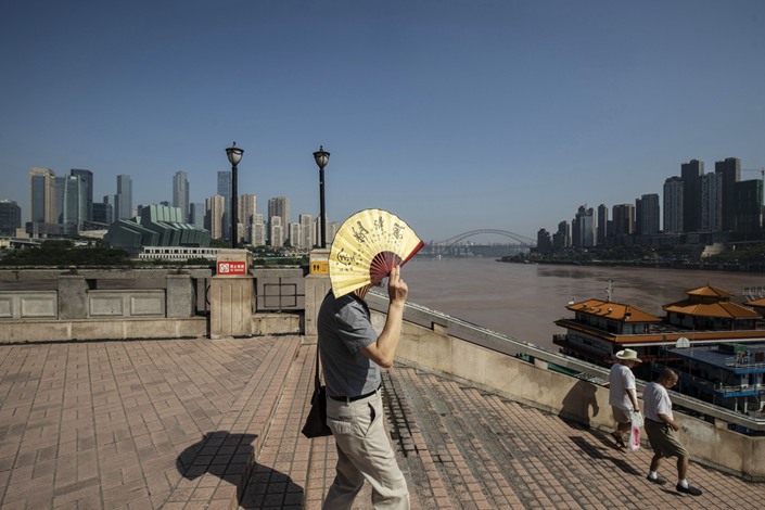 A pedestrian uses a folding fan to shield from the sun as he walks through a square overlooking the Chaotianmen docks in Chongqing on July 28, 2020. Photo: Bloomberg