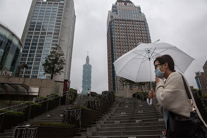 A pedestrian holding an umbrella walks past the Taipei 101 building, center, and other commercial buildings in Taipei, Taiwan, on Jan. 13, 2016. Photo: Bloomberg
