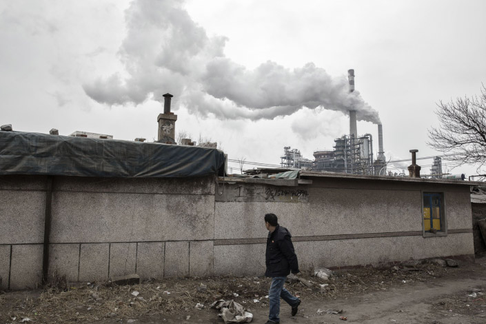 A man walks in a residential neighborhood as smoke billows from the chimneys of a factory nearby in Dalian, Northeast China’s Liaoning province, on Jan. 17.  Photo: Bloomberg