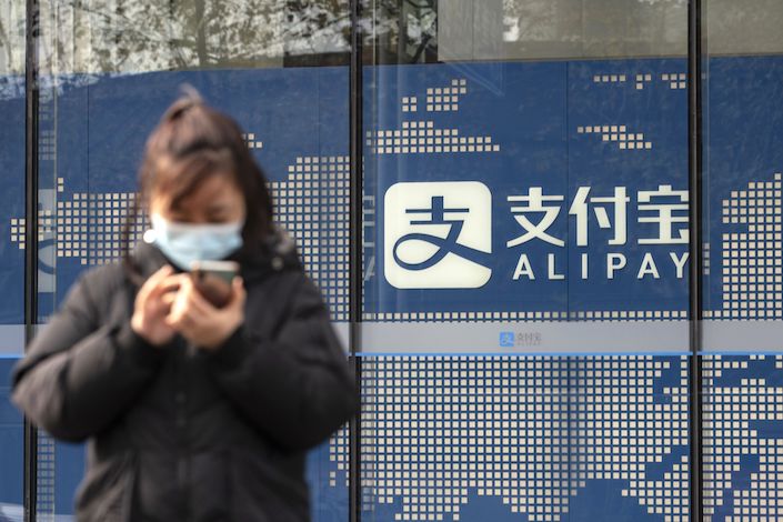 A pedestrian uses a smartphone in front of an Alipay sign outside an Ant Group Co. office building in Shanghai