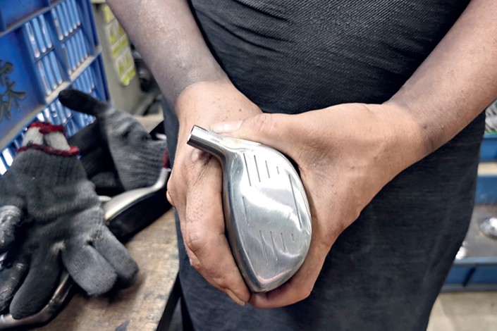 A worker holds a golf clubhead that has been ground and polished by a vibration machine. Photo: Huang Shulun/Caixin