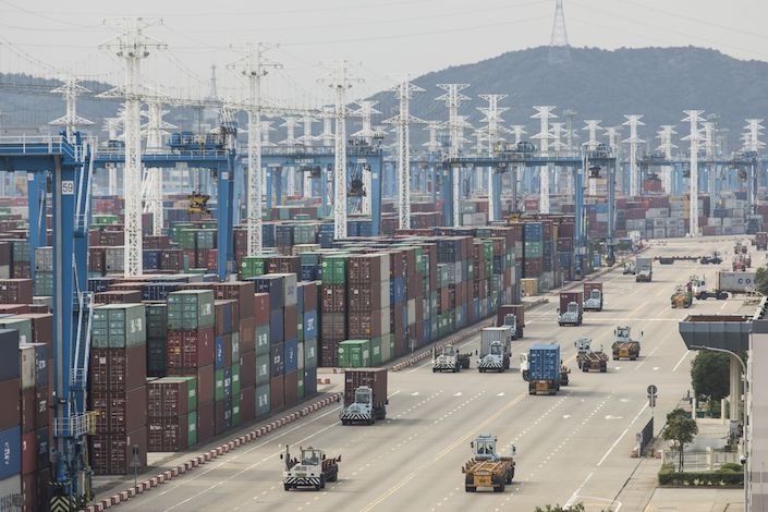 Containers sit stacked next to gantry cranes as trucks operate at the Port of Ningbo-Zhoushan in Ningbo