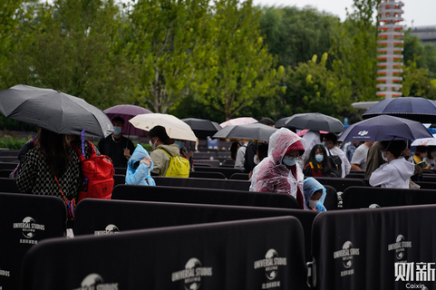 2021年9月20日，北京环球影城门口，身穿雨衣和打伞的游客正在排队。9月20日，北京环球度假区正式开园。出于安全和疫情防控需要，园方于9月19日至21日启动客流管理预案，仅限持当日北京环球影城门票、环球城市大道电影院电影票或有效酒店房间预订证明的游客进入北京环球城市大道，因此园区并没有出现过分拥挤的情况。图/财新实习记者 刘益