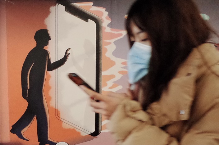 A young woman looks at her mobile phone as she walks past a billboard in Beijing on March 10, 2021. Photo: VCG