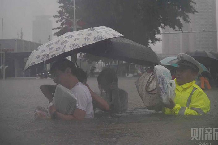People cross a flooded road in Zhengzhou, Central China’s Henan province, on July 20. Photo: Chen Liang/Caixin