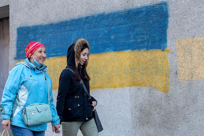 Two women walk past a Ukrainian fag painted on a wall in the center of the second largest Ukrainian city of Kharkiv, located some 40 km from the Ukrainian-Russian border on February 21, 2022