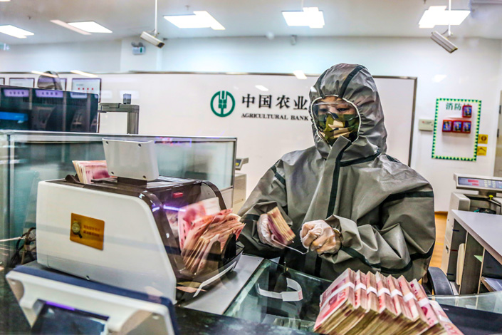 A bank employee counts banknotes while dressed in a protective suit. Photo: VCG