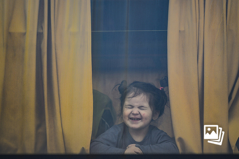 当地时间2022年3月25日，罗马尼亚Isaccea-Orlivka国境线上，一名跟随家人前往邻国避难的乌克兰儿童在大巴窗户前扮鬼脸。联合国儿童基金会在3月24日表示，截至当日已有430万乌克兰儿童流离失所，占该国750万儿童的一半以上。图：Andreea Alexandru/视觉中国