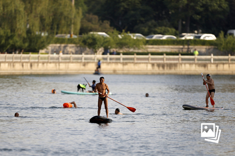 2022年5月22日，北京市东城区，市民在河道内划桨板、游泳。 近几个月，许多城市的河道和湖面上出现了一批“乘风破浪”的市民。他们装束靓丽，踩在色彩鲜艳的直板上，滑行在城市水域中。这种水上运动叫做立式桨板（Stand-up Paddle，简称SUP），源自美国夏威夷地区。近年来，受疫情管控的影响，桨板价格亲民、操作简单、适合城市水面等优点逐渐凸显，受到了越来越多城市人群的青睐。据央视网报道，在2022年暑假开始之前，一家位于北京市顺义奥林匹克公园的水上俱乐部月销量已同比增长了40%-50%。俱乐部桨板业务客流量相比往年提升了一倍还要多。图：富田/中新社