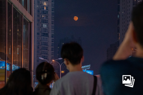 2022年9月10日中秋夜，北京市，一轮圆月跃过云层，出现在高楼之间，市民们举起手机拍照，记录下“团圆之夜”。图：财新 张芮雪