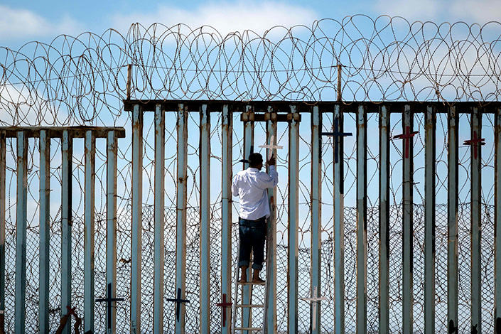 A deported Mexican migrant hangs wooden crosses on the fence at the U.S.-Mexico border in Tijuana, Mexico, on July 4. Photo: VCG