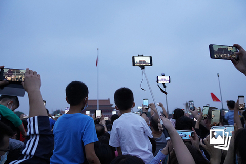 2022年10月1日，北京市，傍晚的天安门广场，两个小朋友坐在父母肩头观看降旗仪式。据新华社报道，国庆日当天，约有21.8万名群众簇拥在天安门广场周围观看升旗仪式。财新发现，傍晚的天安门广场，依旧热度不减，挤满了前来观看降旗仪式的市民。图：财新 丁刚