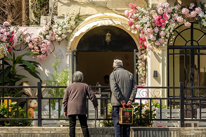 A pair of seniors stop along a street in Shanghai to appreciate a building facade decorated with flowers on March 2. Photo: VCG