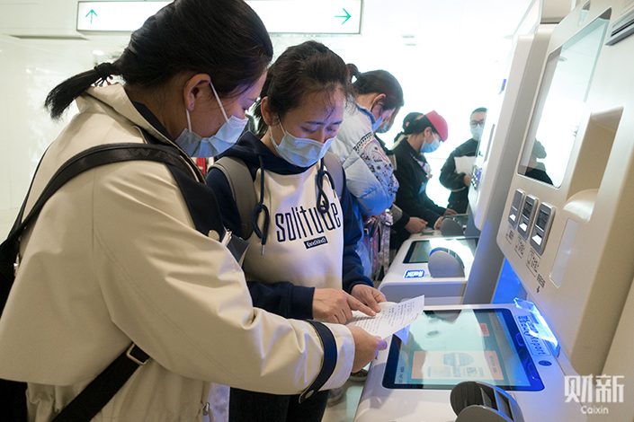 Patient companion, Chen Ting (right), operates a self-service machine in Peking Union Medical College Hospital on March 9, assisting her client from North China’s Inner Mongolia autonomous region in seeking medical treatment. Photo: Ding Ke (intern)/Caixin