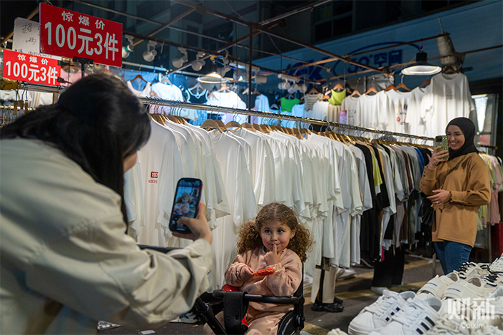 A woman takes photo of a girl in March at a clothing shop in the Binwang night market in Yiwu, East China’s Zhejiang province. Photo: Chen Liang/Caixin