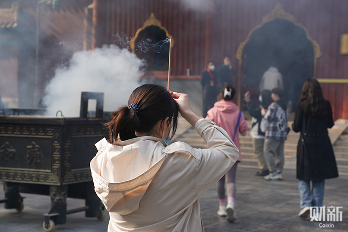 A woman burning incense keels in prayer at Beijing’s Yonghe Temple on April 22. Photo: Sun Muzi (intern)/Caixin
