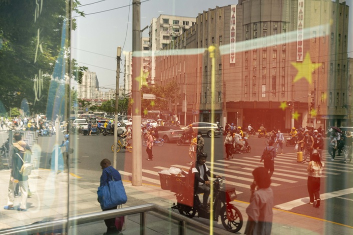 Chinese flags and pedestrians get reflected in a window in Shanghai on June 2. Photo: Bloomberg