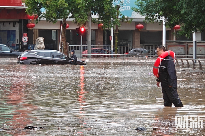 On Monday in Beijing's Mentougou district, a resident wears a safety ring while walking along a flooded road. Photo: Caixin