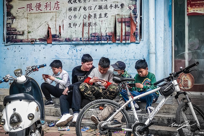 A group of children play mobile games at the entrance of a supermarket in Luohe, Henan, on May 4. Photo: VCG