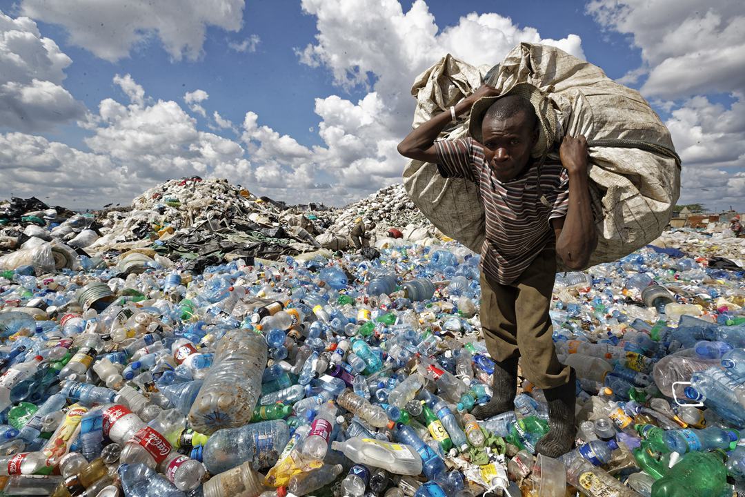 A scavenger climbs over a mountain of plastic bottles on his way to sell a sack of recyclables at a dump in Nairobi, Kenya, in December 2018. Photo: VCG