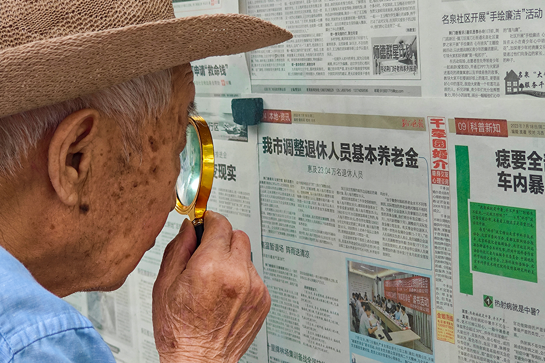 An elderly man uses a magnifying glass to examine the 2023 pension policy in Jingmen, Hubei province, July 18, 2023. Photo: VCG