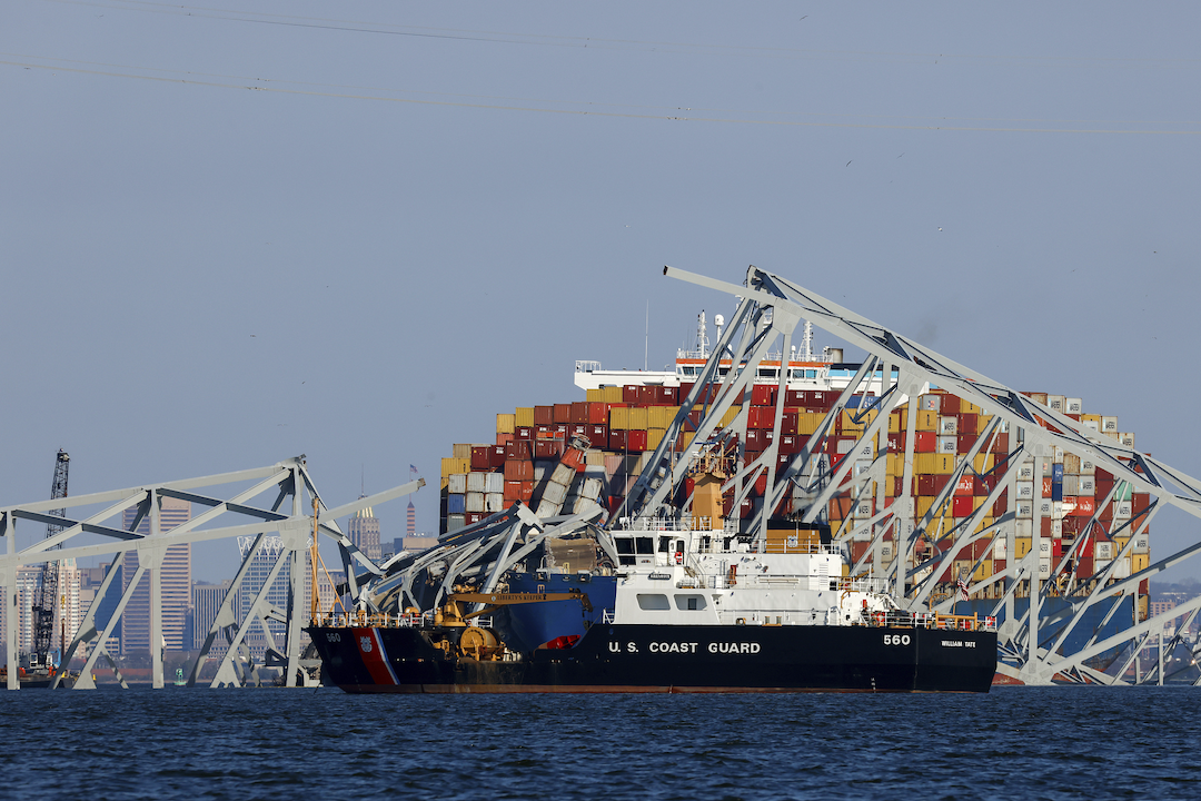 A Coast Guard coastal buoy tender passes by as wreckage of the Francis Scott Key Bridge rests on the container ship Dali, March 30, 2024, in Baltimore